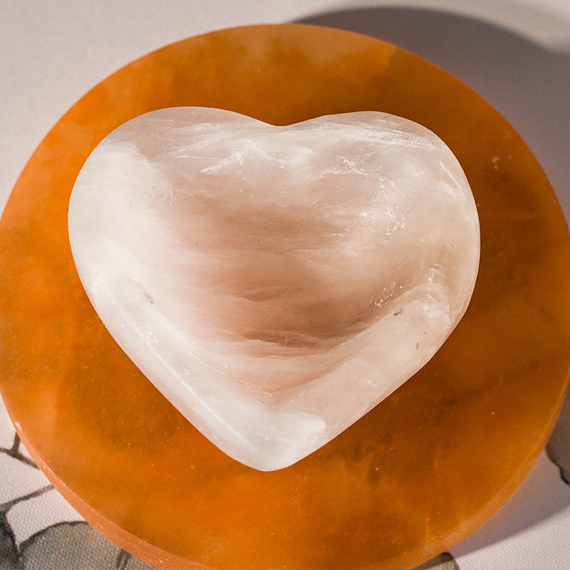 White heart-shaped Selenite Mineral Offering Bowl resting on a warm orange round bowl