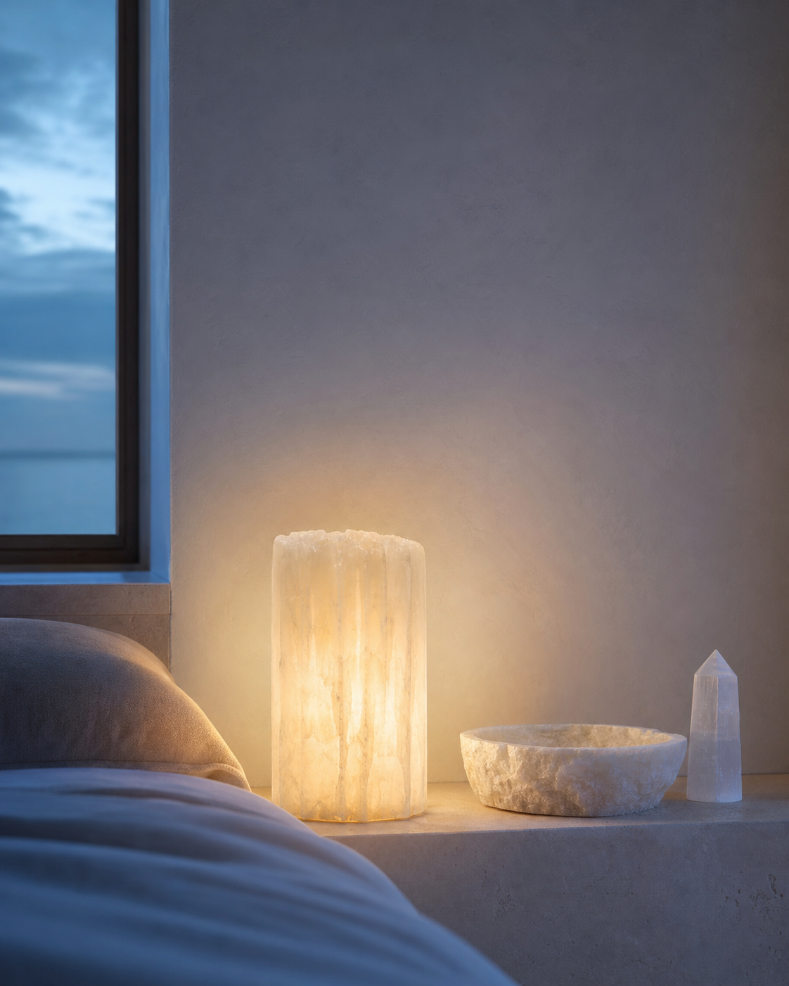 A warm translucent mineral lamp beside a stone bowl at dusk